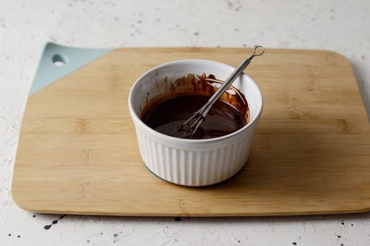 Bol de chocolat fondu avec un fouet sur une planche en bois, prêt pour la préparation de desserts.