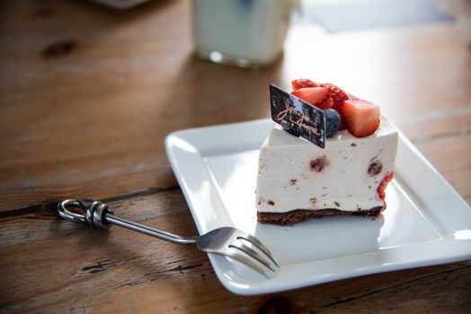 Cheesecake maison sur assiette blanche, décoré de fraises et myrtilles, avec une petite fourchette en métal.