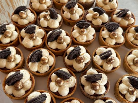 Mini tartelettes au chocolat garnies de crème, décorées de biscuits Oreo et billes dorées.