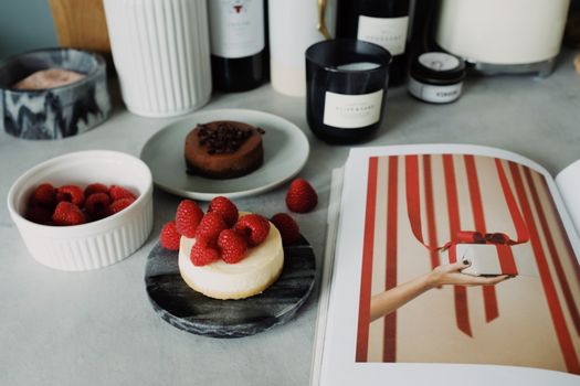 Cheesecake garni de framboises sur un plateau, mini tartelette au chocolat et livre de recettes en arrière-plan.